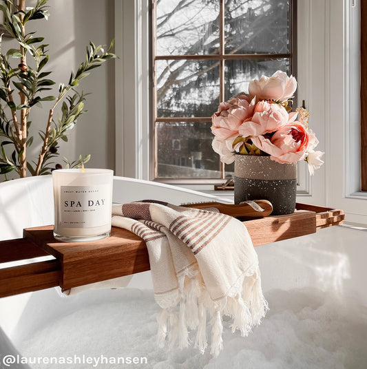 A Turkish cotton hand towel with neutral color stripes is draped over a wooden towel bar in a bathroom setting, alongside a candle and a vase with flowers.