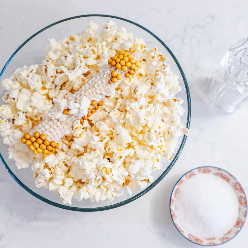 Popped Popcorn in a bowl with the leftover cob on a white marble table with salt