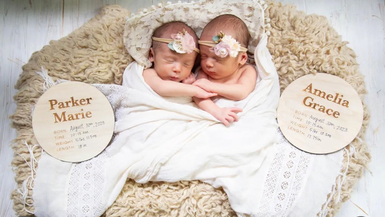 Twin babies with a round birch wood plaque with the engraved text of their names and birthdate