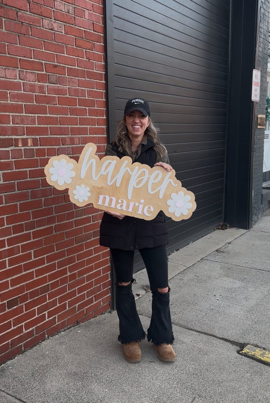 Person holding a sign with 'harper marie' against a brick wall.