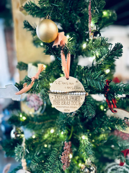A wooden engraved ornament with a Taylor Swift 'Era Tour 2024' inscription, adorned with a frayed chiffon ribbon and displayed on a Christmas tree.