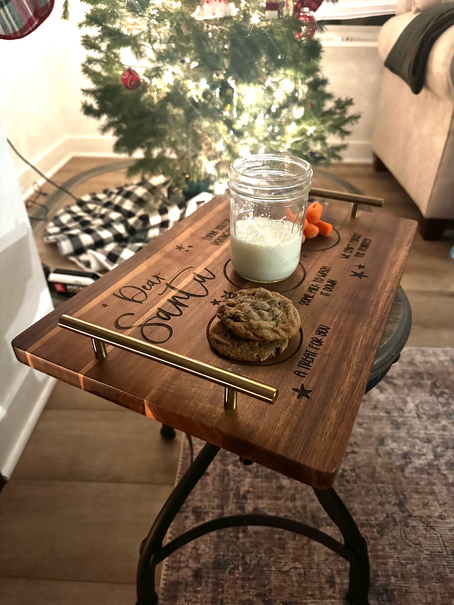 Wooden tray with a glass of milk and cookie on a stool in front of a Christmas tree.