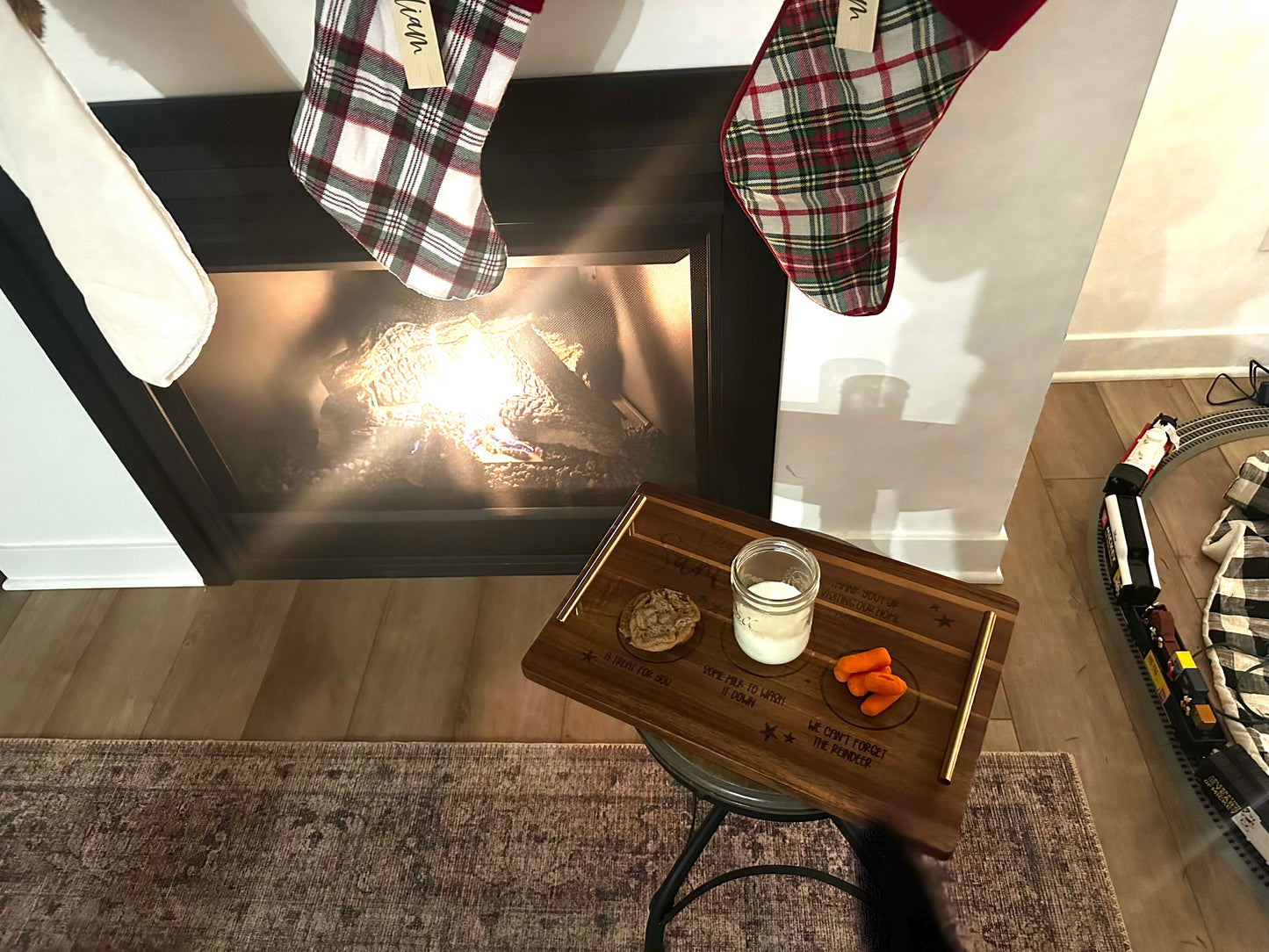 Tray with a glass of water, cookie, and carrot in front of a fireplace with stockings hanging above.