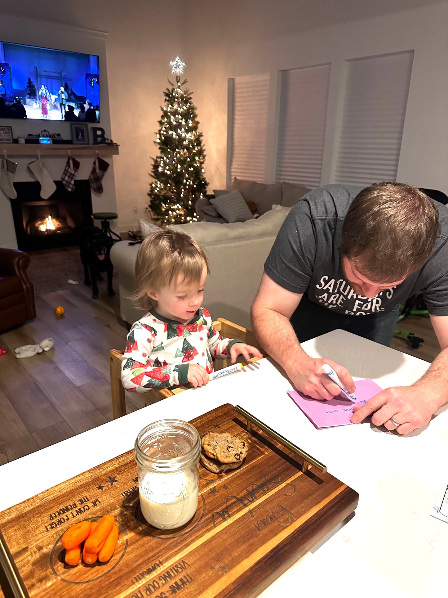 Man and child in a living room with a Christmas tree and fireplace.
