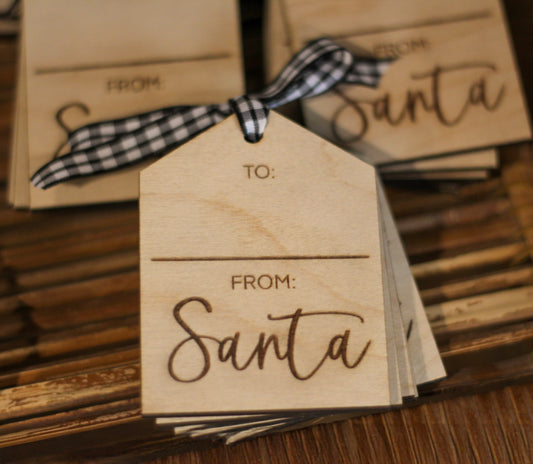 Wooden gift tags with 'From Santa' printed on them, adorned with a black and white checkered bow, set against a backdrop of wooden elements.