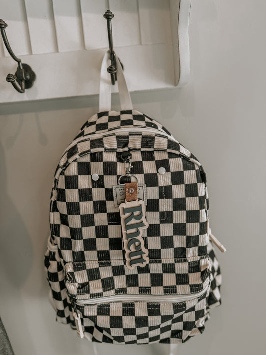 Black and white checkered backpack with 'Rhett' logo hanging on a hook.