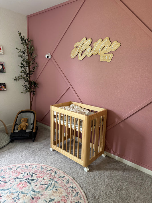 Nursery room with wooden crib, pink wall, and decorative elements.