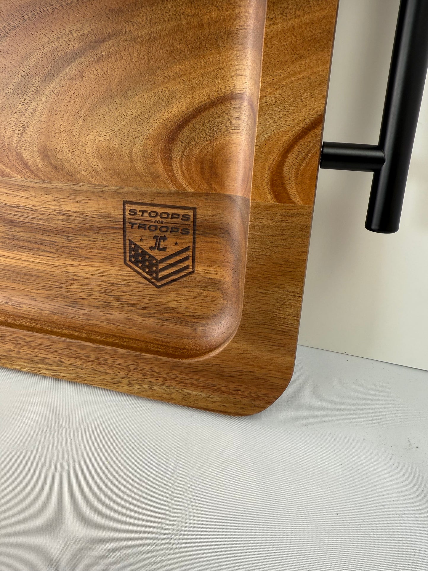 Wooden cutting board with a black handle and engraved logo on a white surface