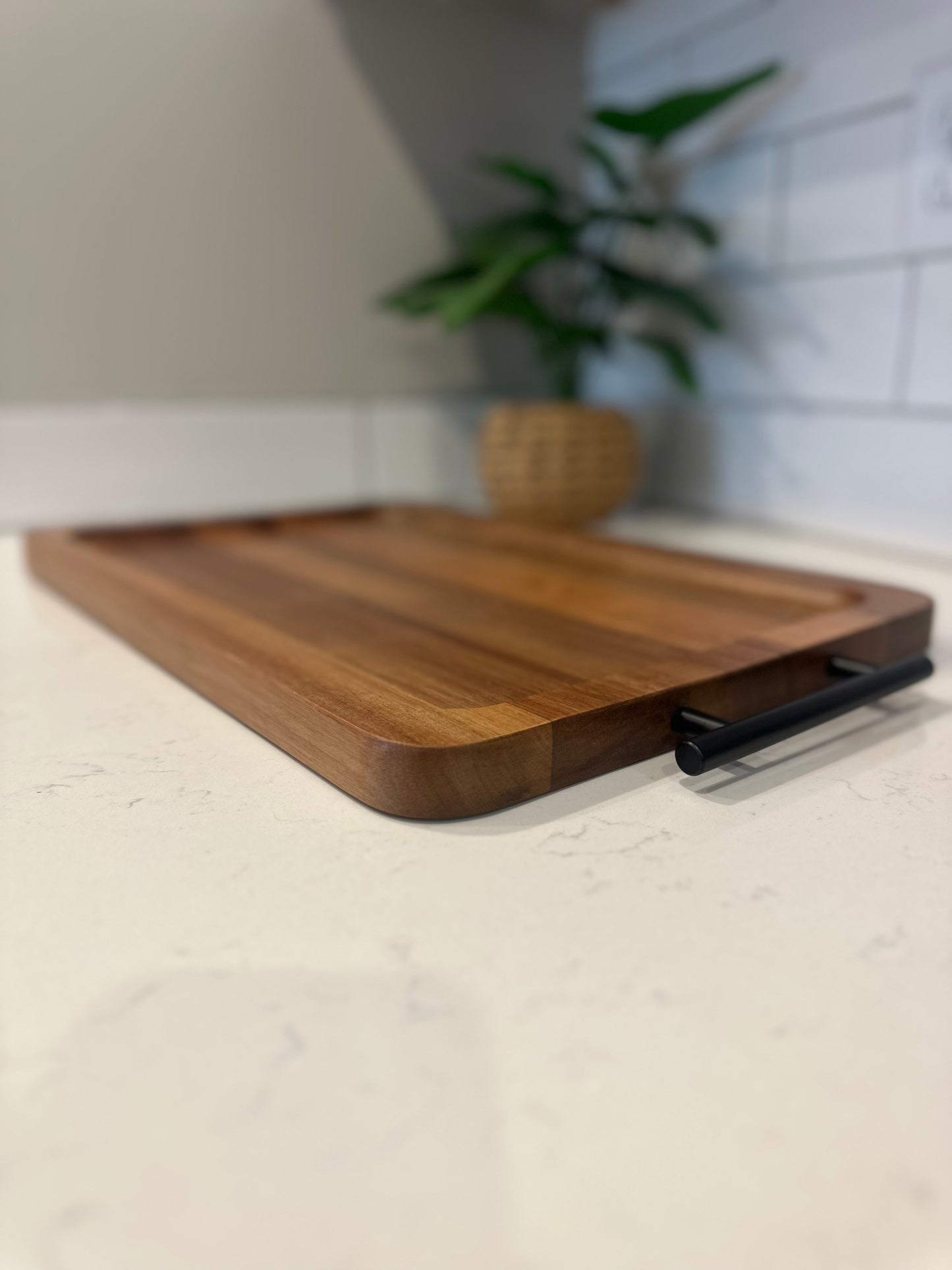 Wooden cutting board with a black handle on a kitchen counter