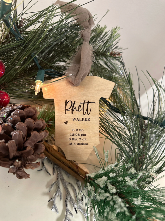 A personalized wooden Christmas ornament with a baby's name and birth details engraved on it, placed among holiday decorations.