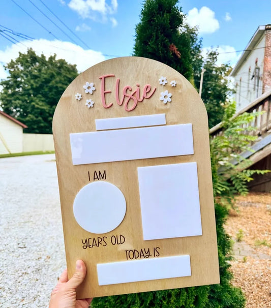 Wooden birthday sign with 'Elsie' written on it, held outdoors.