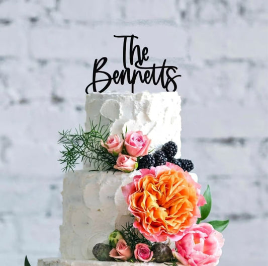 A wedding cake with a white frosting topper that reads 'The Bennetts' on top, decorated with a floral arrangement and berries.