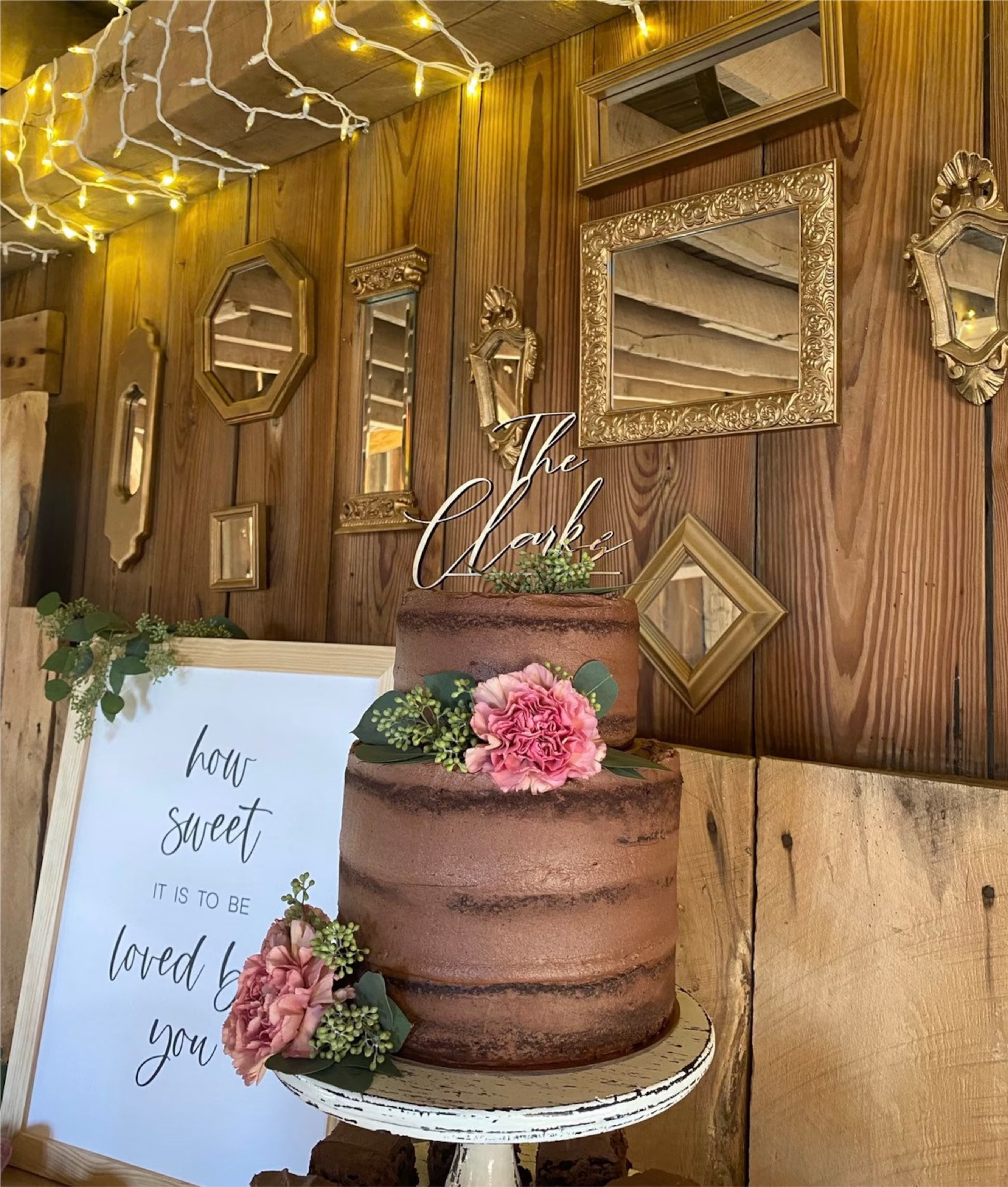 A wedding cake with a white frosting topper that reads 'The Clarks' on top, decorated with a floral arrangement and berries.
