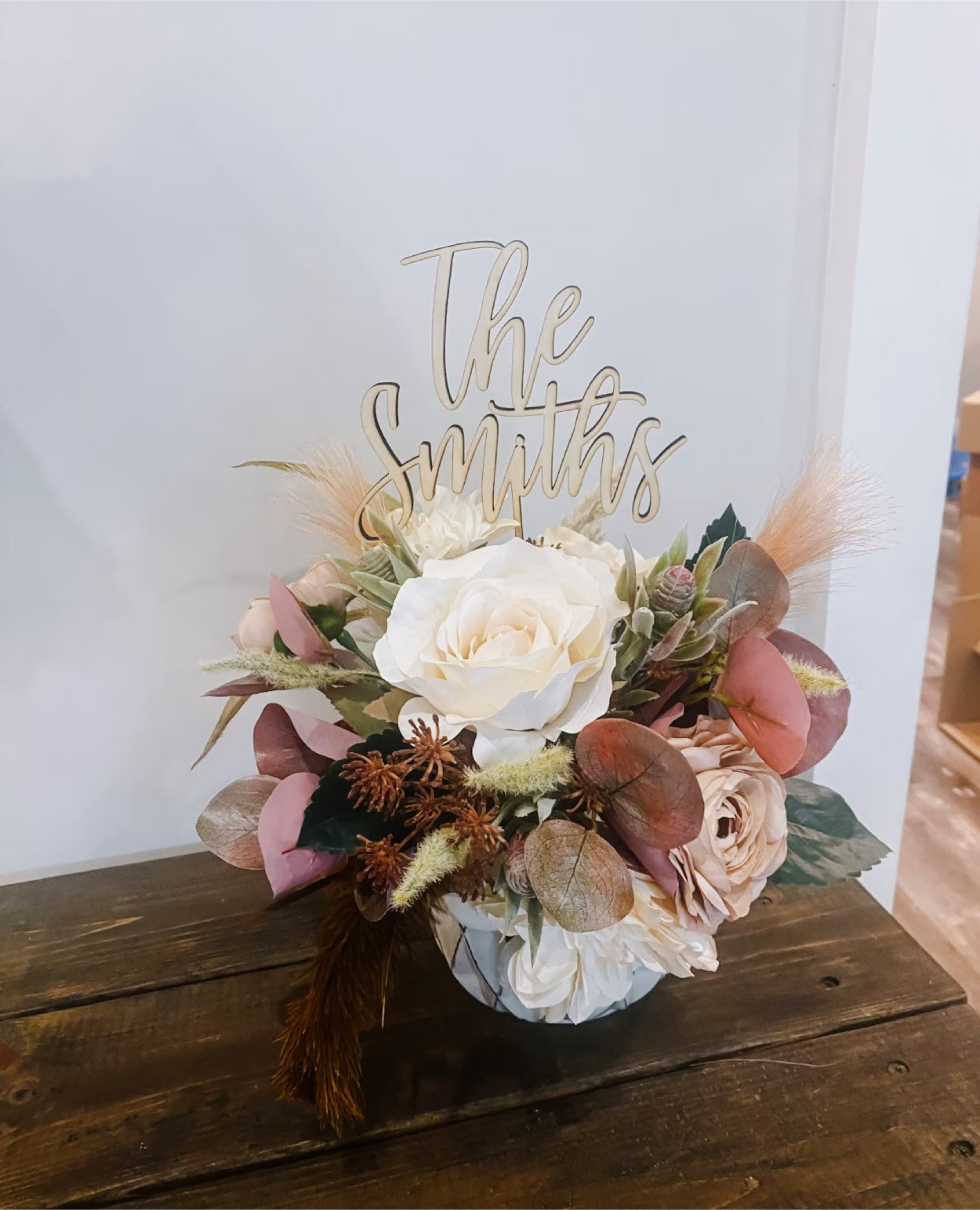 A wedding cake with a white frosting topper that reads 'The Smiths' on top, decorated with a floral arrangement and berries.