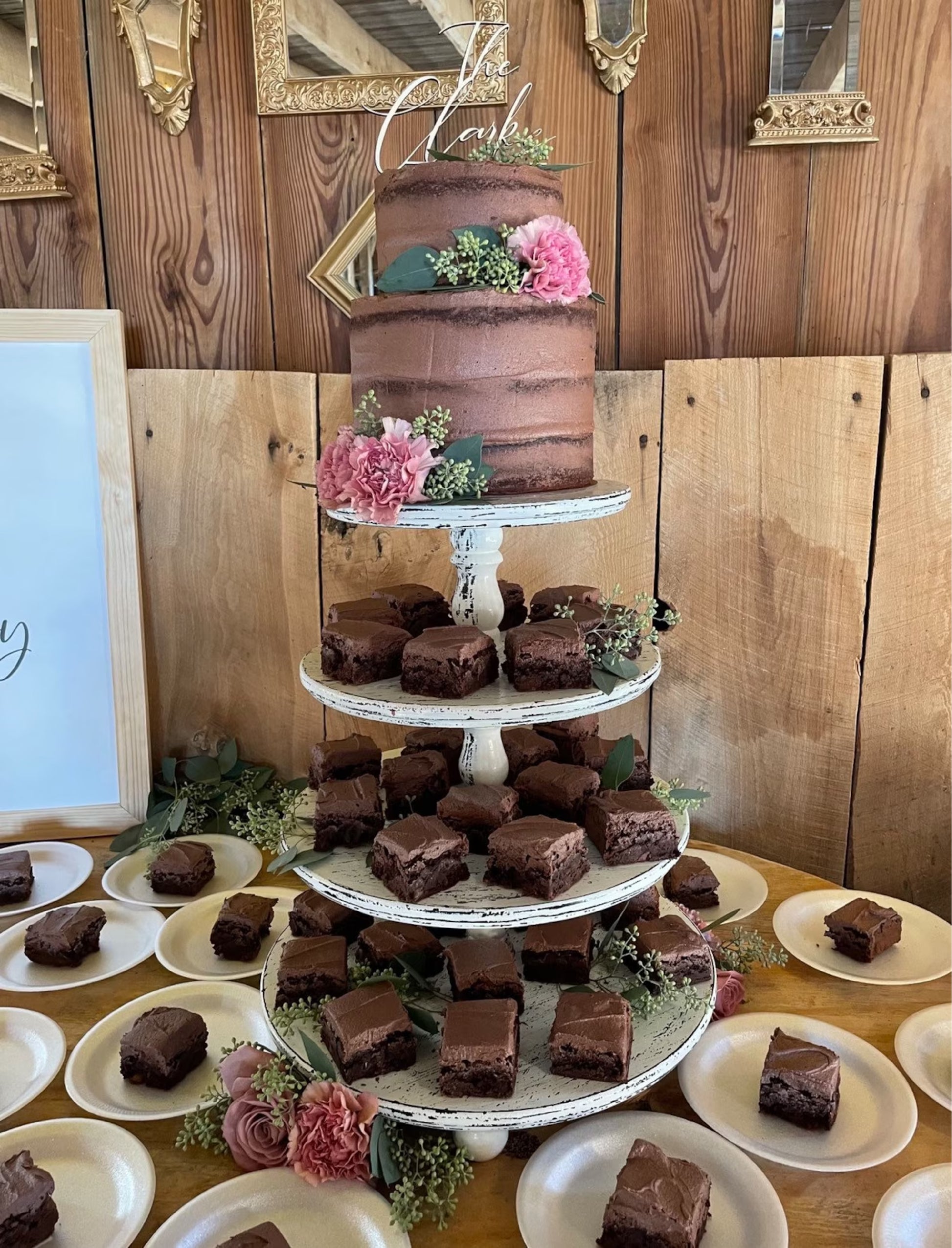 A wedding cake with a white frosting topper that reads 'The Clarks' on top, decorated with a floral arrangement and berries.