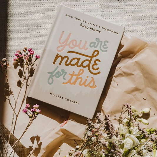 A book titled 'You Are Made For This' by Melissa Horvath placed on a beige surface with a floral arrangement and a quote about being enough.