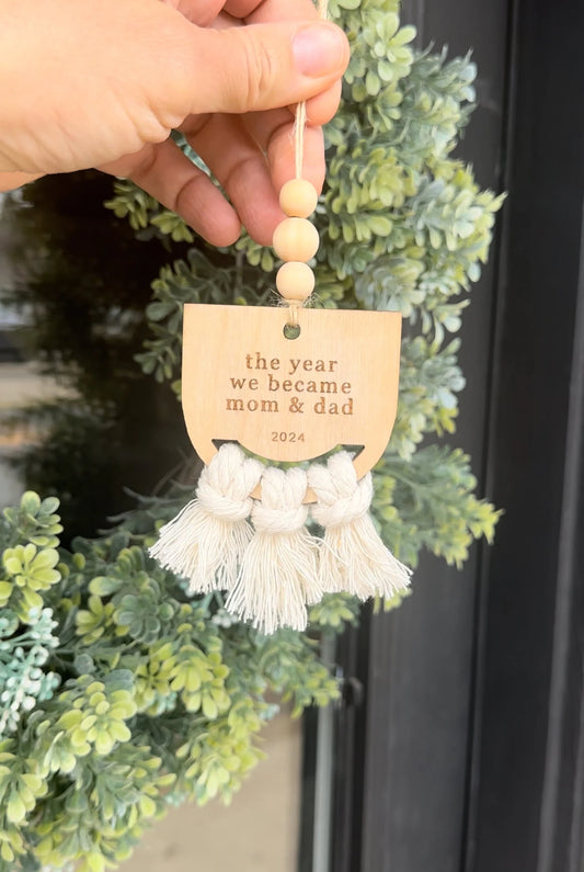 The year we became mom & dad ornament held in front of black door with wreath