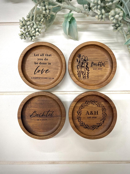 Four personalized wooden ring dishes with various designs, each with a different name and wedding date inscribed on it.