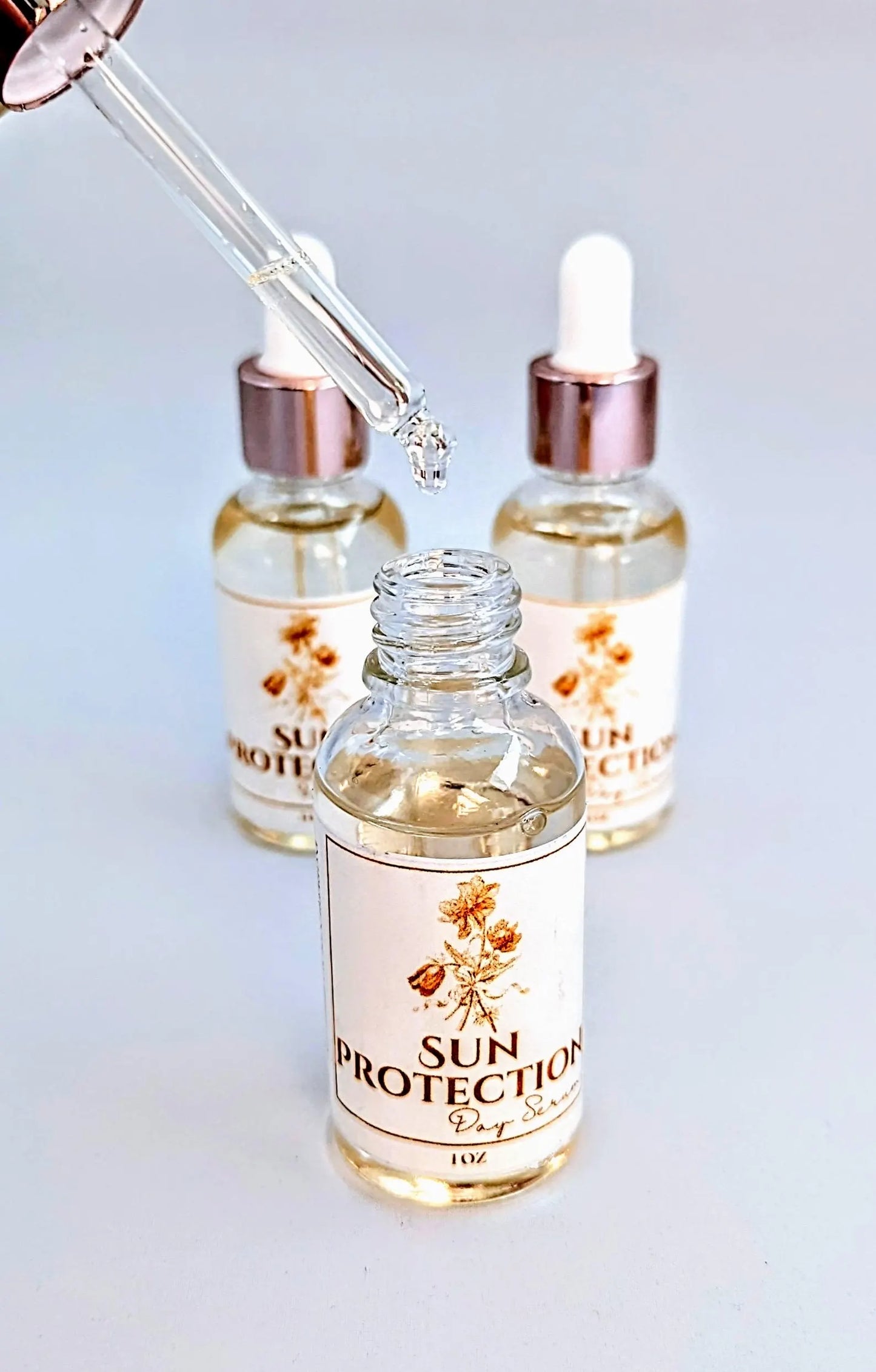 Three bottles labeled 'Sun Protection' with dropper caps, indicating they contain face serum with SPF and rosehip oil for sun protection. Front one open to show whats inside and how to apply