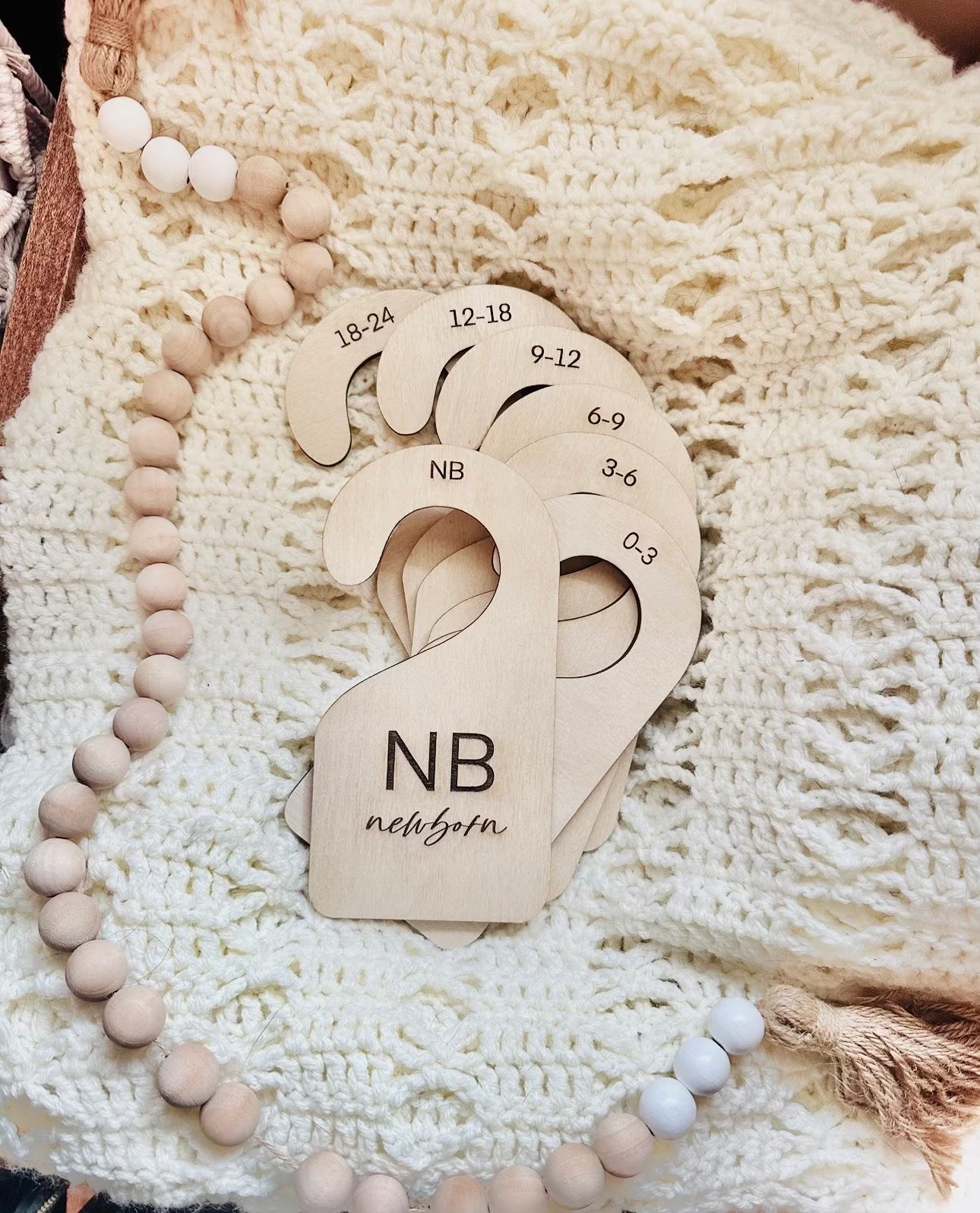 A set of beige baby clothes organizers made of birch wood, with sizes engraved on them, displayed on a knit fabric.