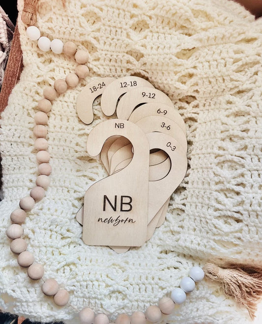 A set of beige baby clothes organizers made of birch wood, with sizes engraved on them, displayed on a knit fabric.