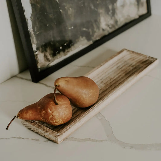A rustic wooden decorative tray with two pears on it, placed on a kitchen counter next to a picture frame.