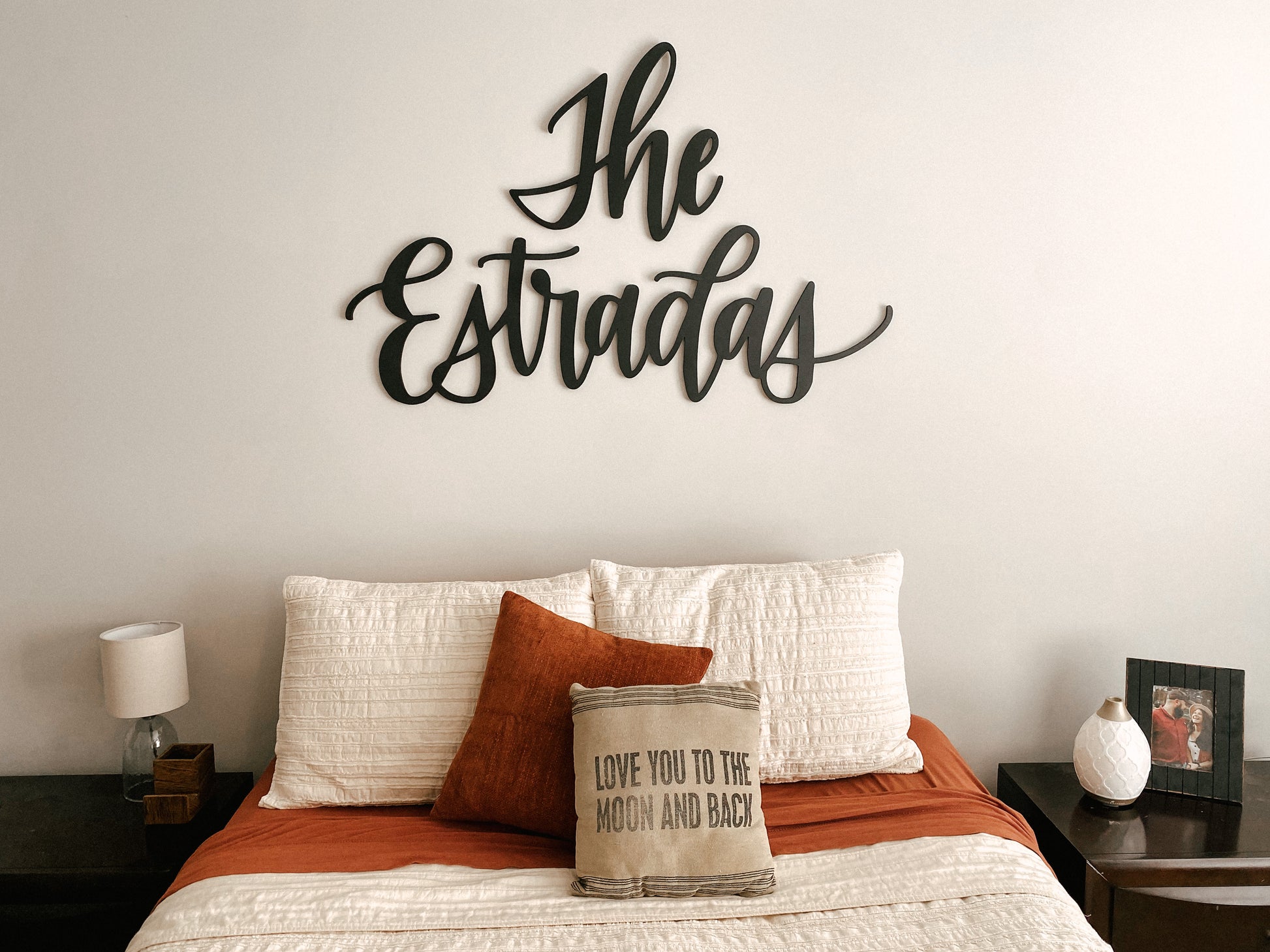 A wooden cutout with the word 'The Estradas' in a large, bold font, mounted on a wall above a bed