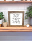 Framed sign with 'Farts are always funny' text on a wooden shelf with plants.