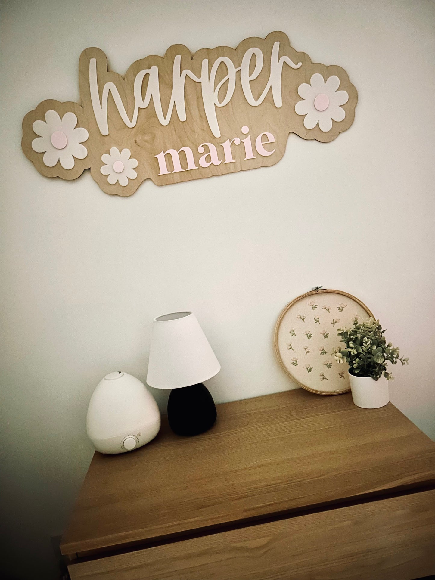 Decorative wall sign with 'harper marie' on a wall above a wooden dresser with decorative items.