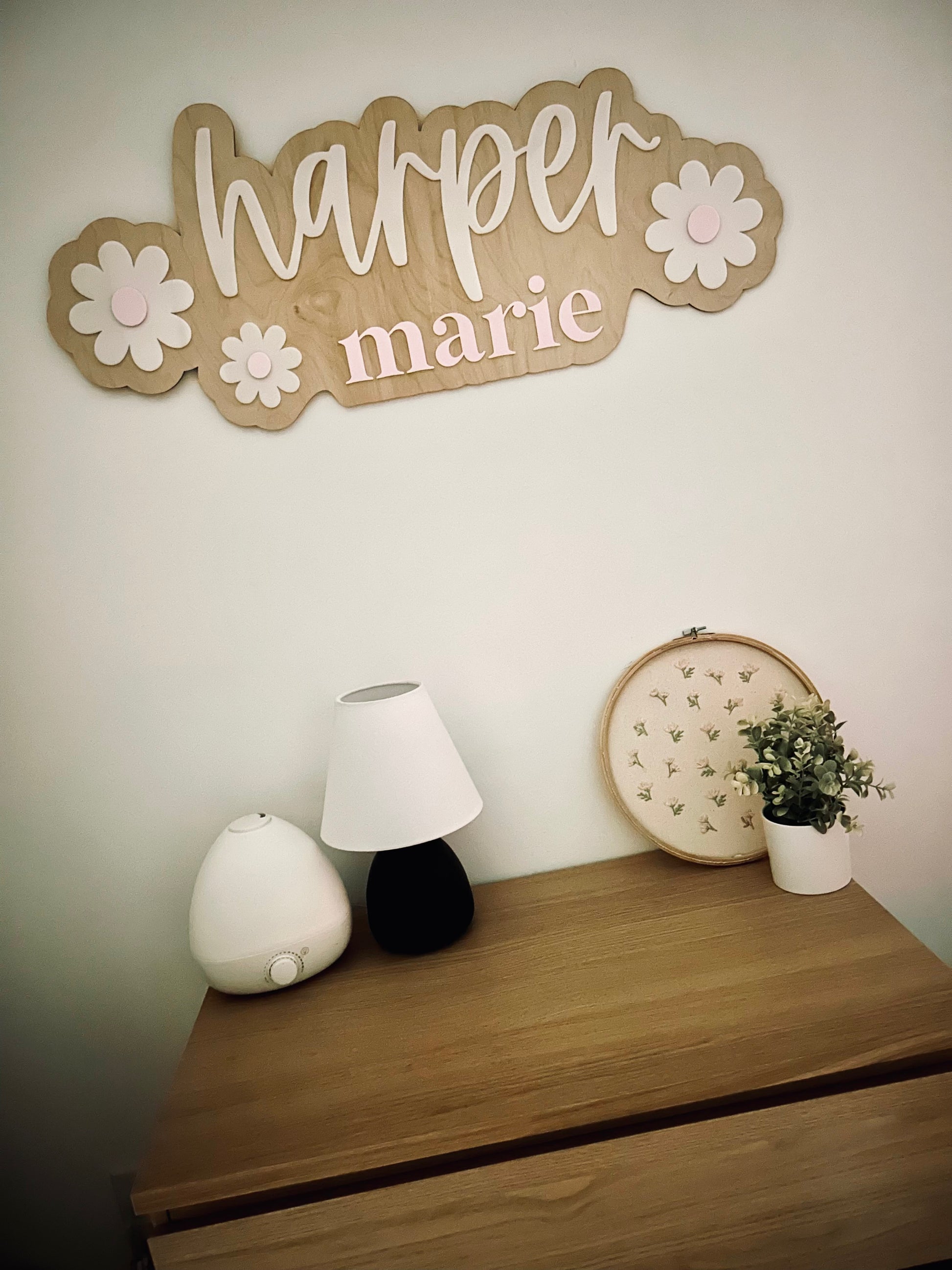 Decorative wall sign with 'harper marie' on a wall above a wooden dresser with decorative items.
