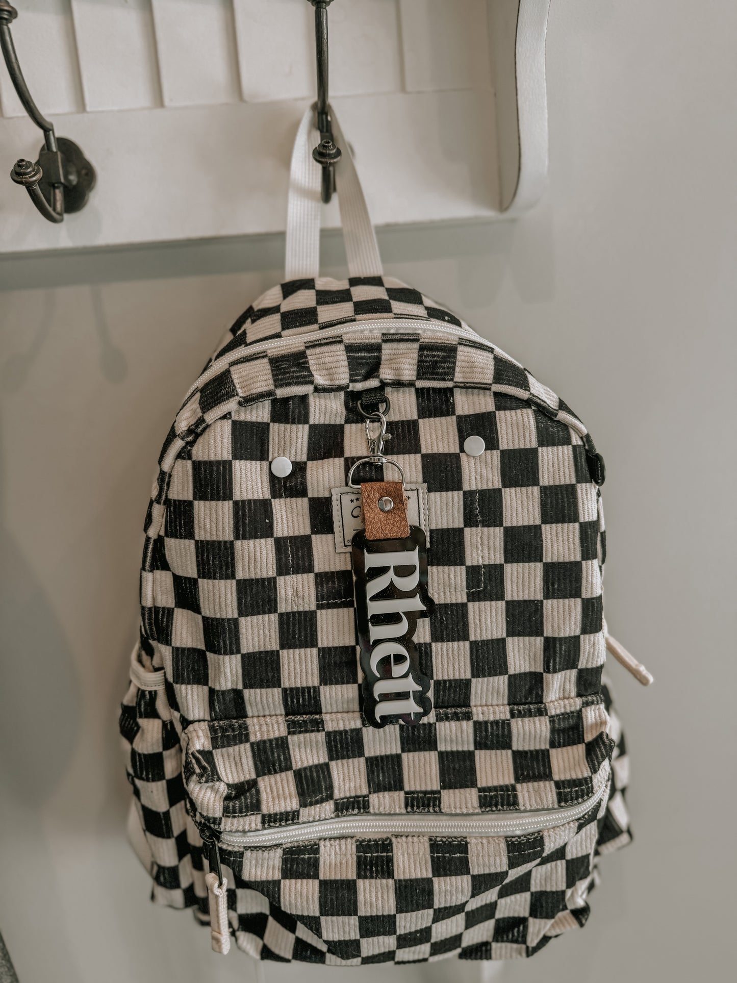 Black and white checkered backpack with 'Rhett' brand tag hanging on a hook.