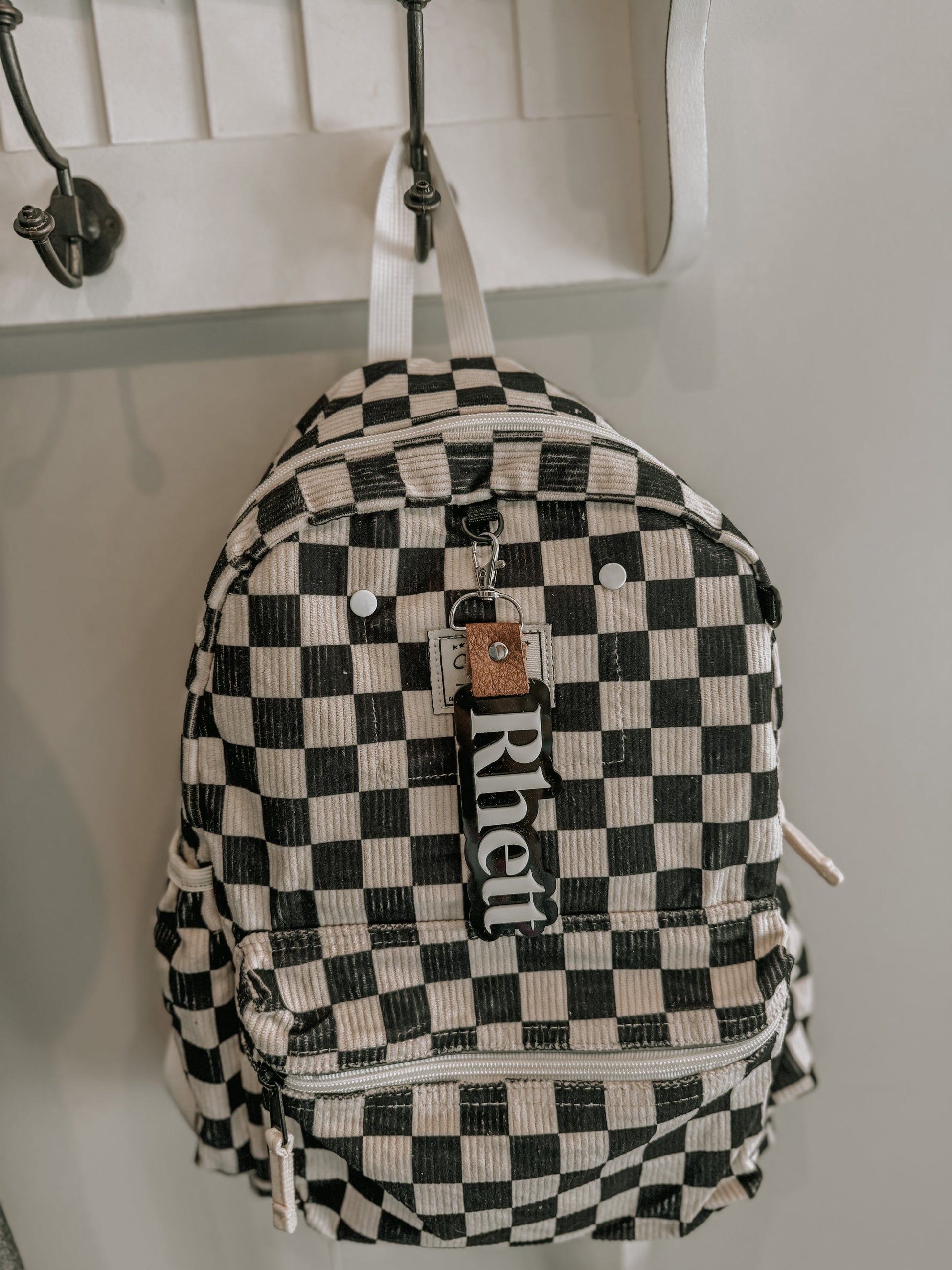 Black and white checkered backpack with 'Rhett' brand tag hanging on a hook.